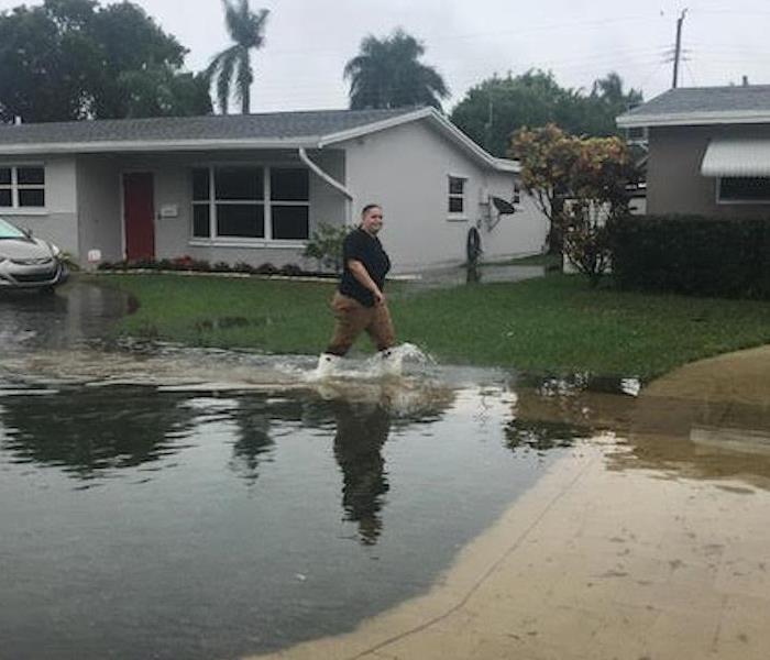 A woman walking through standing water in front of a home. 
