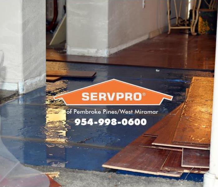 A floor in a home is flooded with water, and some of the hardwood floor has been removed, exposing water damage to the subflo