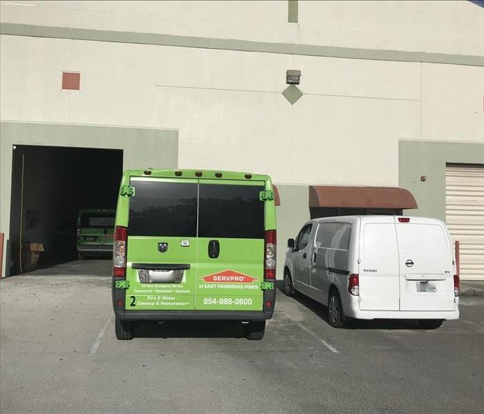 Una camioneta SERVPRO y una camioneta blanca se estacionan frente a un edificio.